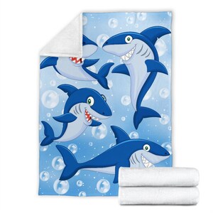 May include: A blue fleece blanket with a cartoon design of four sharks swimming in a blue ocean with white bubbles.