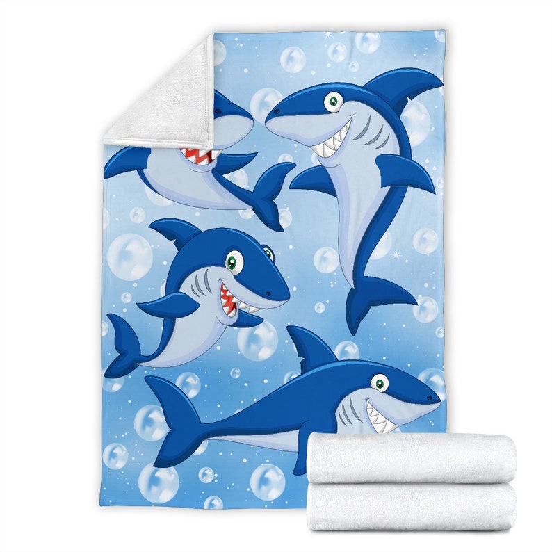 May include: A blue fleece blanket with a cartoon design of four sharks swimming in a blue ocean with white bubbles.