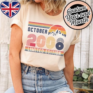 May include: A cream-colored t-shirt featuring a retro-style graphic with the text OCTOBER 2008 LIMITED EDITION. The design includes a sunset, mountain peaks, and horizontal stripes in shades of red, orange, yellow, green, and blue.