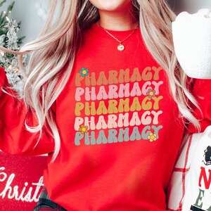 May include: Red sweatshirt with the word "Pharmacy" repeated five times in a rainbow of colors with a flower design next to each word.