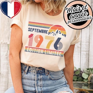 Peut inclure: Un t-shirt couleur crème arborant un graphisme de style rétro avec le texte "SEPTEMBRE 1976" et "ÉDITION LIMITÉE". Le motif comprend un coucher de soleil avec des rayures horizontales, des silhouettes de montagnes et le mot "Est".