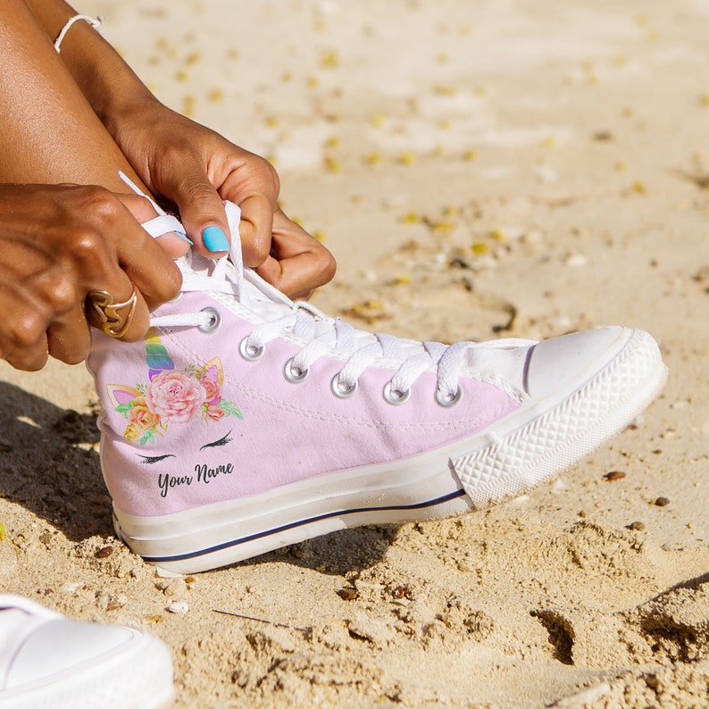 May include: Pink high-top canvas sneakers with a unicorn and floral design. The shoes have white laces and a white rubber sole. The text "Your Name" is printed on the side of the shoe.