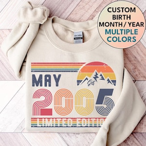 Puede incluir: Sudadera color crema con un diseño retro. El diseño incluye el texto "MAY 2005 LIMITED EDITION" con una franja arcoíris, un gráfico de montaña y las palabras "Custom Birth Month/Year Multiple Colors".
