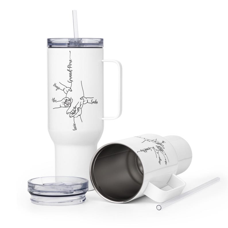 May include: White insulated tumbler with a handle, straw, and lid. The tumbler features a black line drawing of hands holding each other, with the word "Grand-Pere" and names. One tumbler is upright, and another is lying on its side.