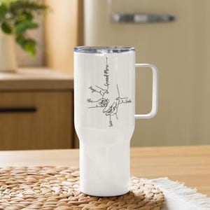 May include: White travel mug with a handle and a clear lid. The mug features a black line drawing of hands and the text "Grand-Mere" with names like Hugo, Alex, and Lucie.