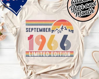 May include: A cream-colored t-shirt featuring a retro-style graphic with the text SEPTEMBER 1966 LIMITED EDITION. The design includes a sunset, mountain peaks, and horizontal stripes in red, orange, yellow, and blue, with a distressed texture.