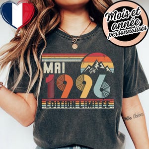 May include: Dark grey t-shirt with a retro design featuring the word "MAI" above the number "1996" in a vintage font. The design includes a mountain graphic and the words "EDITION LIMITEE". A French flag heart is in the upper left corner.