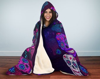 May include: A hooded blanket with a dark purple background and a colorful sugar skull design. The blanket is made of soft, plush fabric and features a large hood.