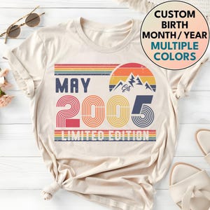 May include: Cream-colored t-shirt with a retro design featuring the word "MAY" above the number "2005" in red and orange. The design includes a mountain graphic and the text "LIMITED EDITION". A circular graphic says "CUSTOM BIRTH MONTH/YEAR MULTIPLE COLORS".