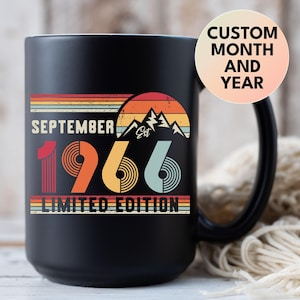 May include: A matte black ceramic mug featuring a retro-style graphic with the text SEPTEMBER 1966 LIMITED EDITION. The design includes a sunset over mountain peaks in shades of red, orange, and blue, with a circular badge stating CUSTOM MONTH AND YEAR.