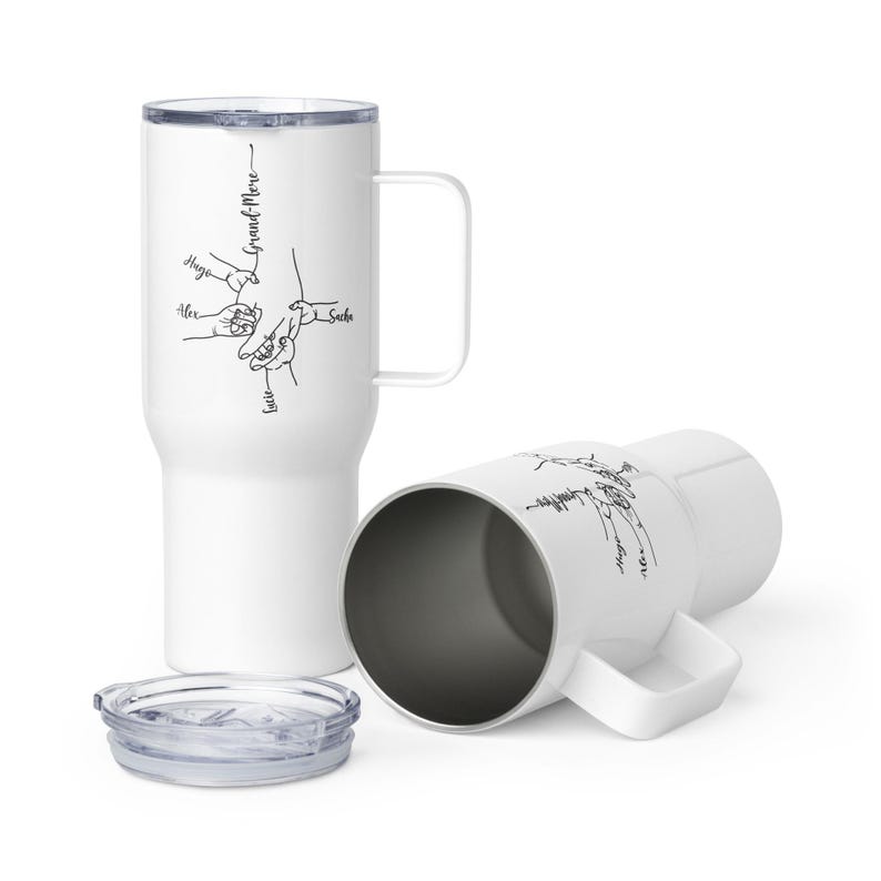 May include: White travel mug with a handle and a lid. The mug features a black line drawing of hands holding each other, with the words "Grand-Mere" and names like "Hugo" and "Alex". One mug is upright, and another is on its side.