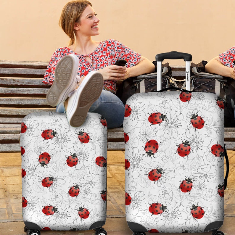 May include: Two white luggage covers with a pattern of red ladybugs and black outlines of flowers on a white background.