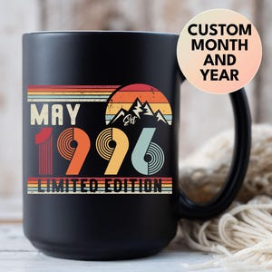May include: Black ceramic mug with a retro design. The mug features the text "MAY 1996 LIMITED EDITION" in a vintage style, with a mountain graphic and the words "Custom Month and Year" on a circular sticker.
