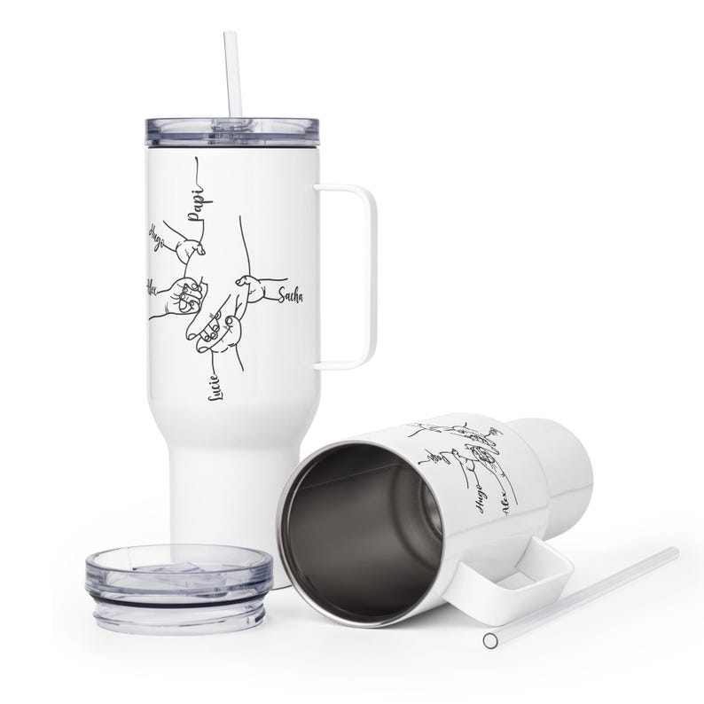 May include: White insulated tumbler with a handle, straw, and lid. The tumbler features a black line drawing of hands holding each other, with names like "Papi," "Hugo," "Sacha," and "Lucie" written on it. Another tumbler is lying on its side.