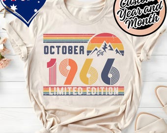 May include: A cream-colored t-shirt featuring a graphic print with the text OCTOBER 1966 LIMITED EDITION. The design includes a retro-style sunset, mountain silhouette, and horizontal stripes in shades of red, orange, yellow, and blue.