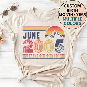 Op de afbeelding: Crèmekleurig T-shirt met een retro design. Het ontwerp bevat de tekst "JUNE 2005 LIMITED EDITION" met een kleurrijke zonsondergangafbeelding. Een cirkelvormig ontwerp toont "CUSTOM BIRTH MONTH/YEAR MULTIPLE COLORS".