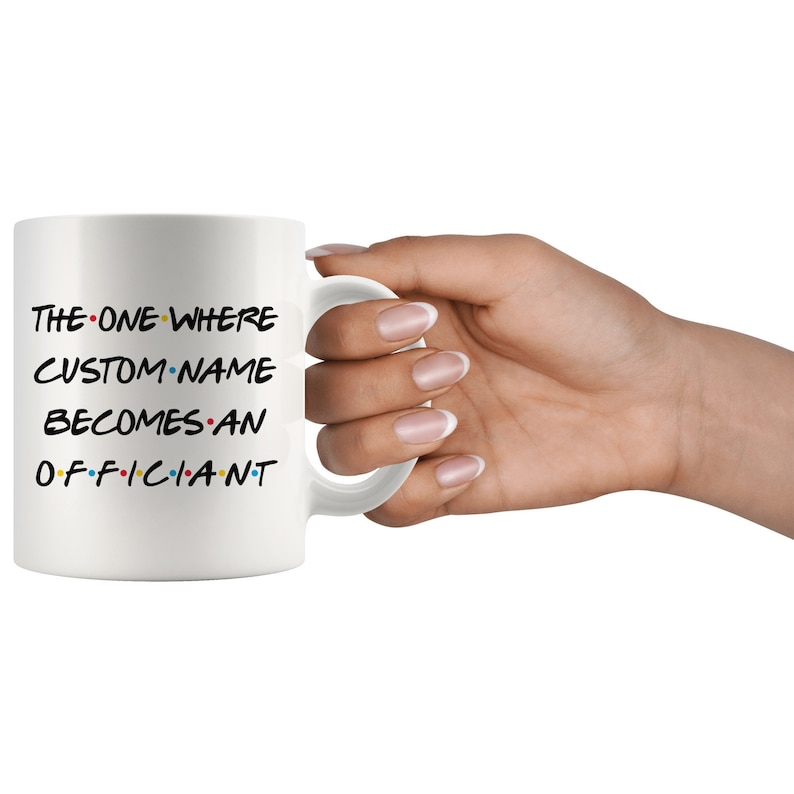 K&ouml;nnte beinhalten: Wei&szlig;e Keramiktasse mit schwarzem Text, der "THE ONE WHERE CUSTOM NAME BECOMES AN OFFICIANT" lautet, mit bunten Punkten zwischen den W&ouml;rtern.