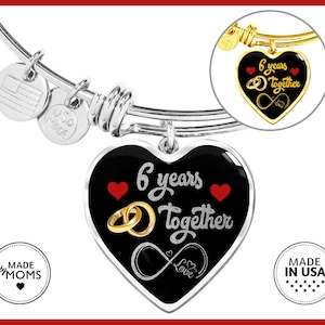 May include: A silver charm bracelet with a black heart charm that says "6 years together" with a gold infinity symbol and the word "love". The charm also has two red hearts and two gold rings. The bracelet has a silver tag that says "Made by Moms" and a silver tag that says "USP since 2005".