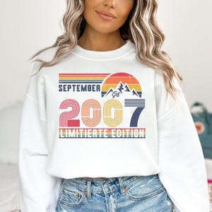 K&ouml;nnte beinhalten: Wei&szlig;es Sweatshirt mit Retro-Design und dem Text "SEPTEMBER 2007 LIMITED EDITION". Das Design beinhaltet eine Berg-Grafik und ein Farbschema im Sonnenuntergangsstil mit Rot-, Orange-, Gelb- und Blaut&ouml;nen.