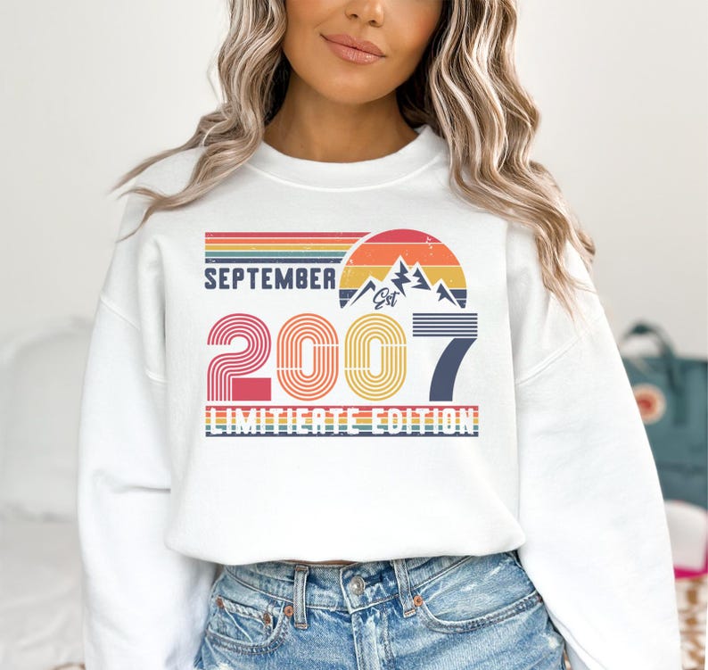 K&ouml;nnte beinhalten: Wei&szlig;es Sweatshirt mit Retro-Design und dem Text "SEPTEMBER 2007 LIMITED EDITION". Das Design beinhaltet eine Berg-Grafik und ein Farbschema im Sonnenuntergangsstil mit Rot-, Orange-, Gelb- und Blaut&ouml;nen.