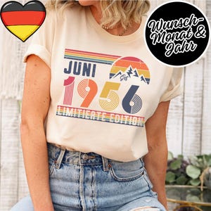 Könnte beinhalten: Cremefarbenes T-Shirt mit Retro-Design. Das Design zeigt das Wort "JUNI" über der Zahl "1956" in Rot und Orange. Das Design enthält einen Regenbogen, Berge und die Worte "LIMITED EDITION". Ein Herz mit der deutschen Flagge befindet sich oben links.