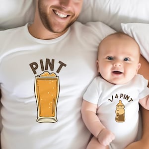 以下が含まれることがあります： お揃いのグラフィックが施された白いTシャツ。片方のシャツには「PINT」の文字とビールのパイントが描かれています。もう一方のシャツには哺乳瓶のグラフィックと「1/4 PINT」の文字が描かれています。