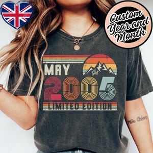 Puede incluir: Camiseta gris oscuro con un diseño retro. El diseño presenta el texto "MAY 2005 LIMITED EDITION" con un gráfico de montaña y una combinación de colores de puesta de sol. La camiseta tiene un aspecto vintage y desgastado.