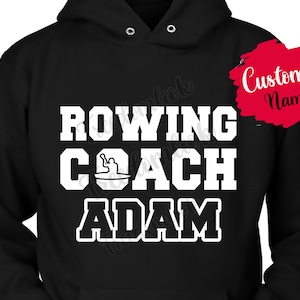 Puede incluir: Sudadera con capucha negra con texto blanco que dice "Rowing Coach Adam" y un pequeño gráfico de una persona remando. Hay un cuadro rojo con texto blanco que dice "Custom Name" en la esquina superior derecha.