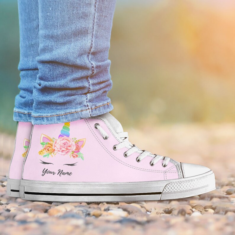 May include: Pink high-top canvas shoes with a unicorn design featuring a rainbow horn, flowers, and eyelashes. The shoes have white laces and a white rubber sole. The text "Your Name" is printed on the shoes.