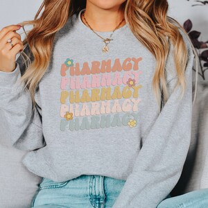 May include: Gray sweatshirt with the word "Pharmacy" repeated five times in a retro font with colorful flowers. The word "Pharmacy" is in different colors in each repetition.