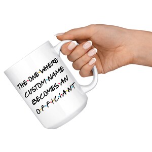 K&ouml;nnte beinhalten: Eine wei&szlig;e Keramiktasse mit einer schwarz-wei&szlig;en Grafik, auf der "The One Where Custom Name Becomes An Officiant" steht.