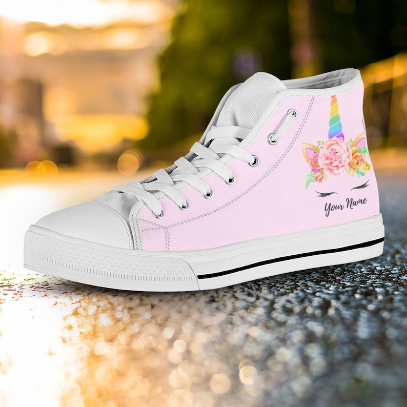 May include: Pink high-top canvas shoes with a unicorn face design. The unicorn has a rainbow horn, flowers, and eyelashes. The text "Your Name" is printed below the unicorn.