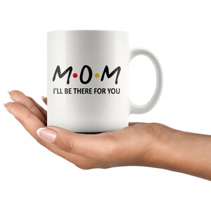 May include: White ceramic coffee mug with black text that reads "M.O.M. I'll be there for you".