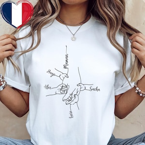 May include: White t-shirt with a black line drawing of a parent's hand holding the hands of four children. The names "Hugo", "Alex", "Sacha", and "Lucie" are written near the children's hands. The word "Maman" is written above the parent's hand.