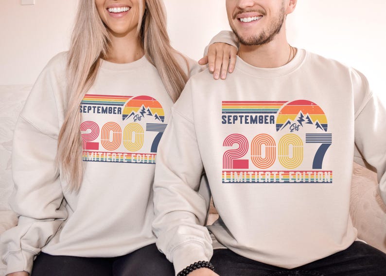 K&ouml;nnte beinhalten: Beige Sweatshirts mit einem Retro-Design mit dem Text "SEPTEMBER 2007 LIMITED EDITION" in einer farbenfrohen, geschichteten Schriftart. Das Design beinhaltet eine Berg-Grafik und einen Regenbogenbogen.