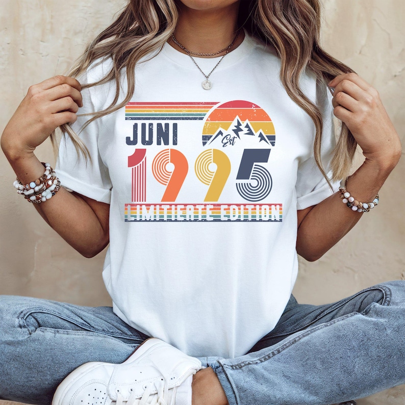 May include: White t-shirt with a retro design featuring the text "JUNI 1995" in a colorful, vintage style. The design includes a mountain silhouette and the words "LIMITIERTE EDITION".