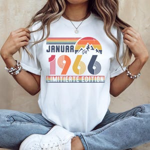 May include: White t-shirt with a retro design featuring the text "JANUARY 1966" in a colorful, vintage font. The design includes a mountain range and a sunset graphic, with the words "LIMITED EDITION" below.