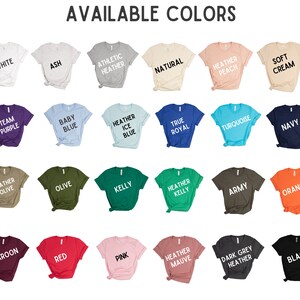 Op de afbeelding: Een display van t-shirts in verschillende kleuren, waaronder wit, as, athletic heather, naturel, heather peach en soft cream. Andere kleuren zijn team paars, babyblauw, heather ice blue, true royal, turquoise en marine. De tekst "AVAILABLE COLORS" staat bovenaan.