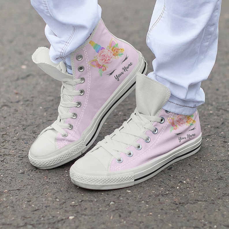 May include: Pink high-top canvas sneakers with a unicorn and floral design. The shoes have white laces and a white rubber sole. The text "Your Name" is printed on the side of each shoe.