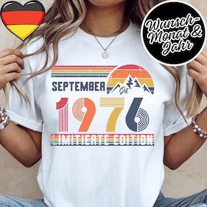 May include: A white t-shirt featuring a retro-style graphic with the text SEPTEMBER 1976, a mountain silhouette, and a sunset design. The graphic includes horizontal stripes in muted colors and the words LIMITED EDITION in a bold, sans-serif font.