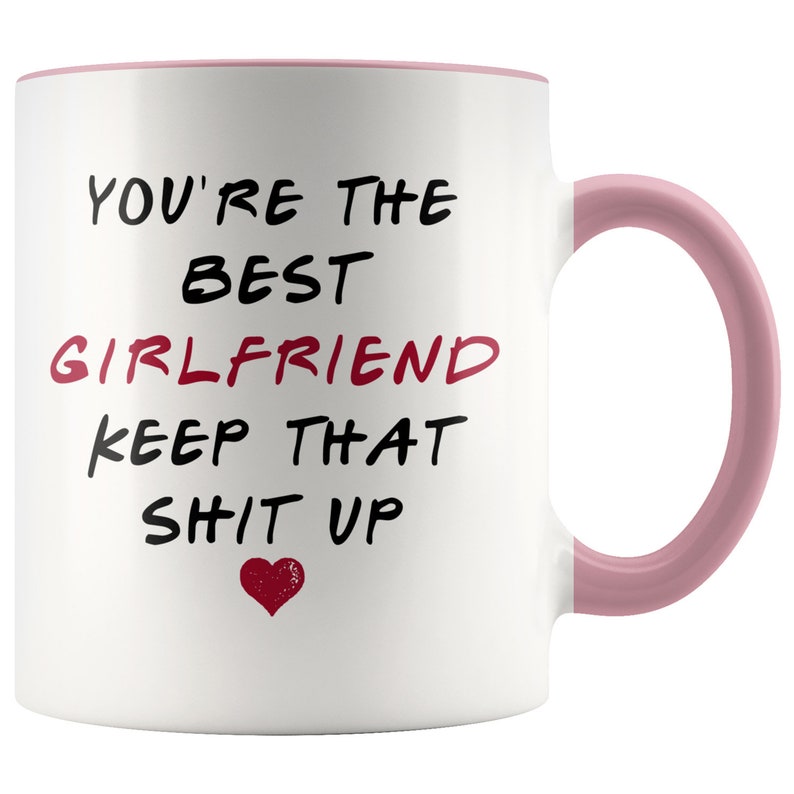 May include: White ceramic coffee mug with a pink rim and handle. The mug has black text that reads "You're the best girlfriend keep that sh*t up" with a red heart at the bottom.