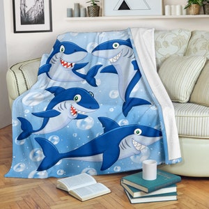 May include: A blue fleece throw blanket with a cartoon design of four smiling sharks swimming in a blue ocean with white bubbles.
