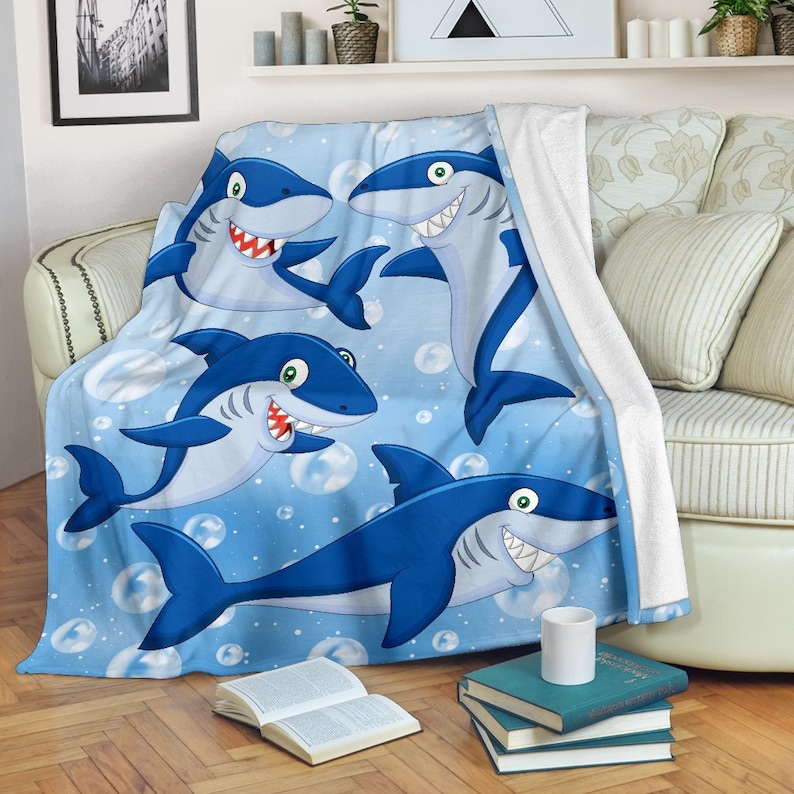 May include: A blue fleece throw blanket with a cartoon design of four smiling sharks swimming in a blue ocean with white bubbles.