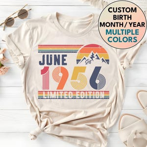 Könnte beinhalten: Cremefarbenes T-Shirt mit Retro-Design. Es zeigt den Text "JUNE 1956 LIMITED EDITION" mit einem Regenbogenstreifen, einer Berg-Grafik und der Option für einen individuellen Geburtsmonat, Jahr und mehrere Farben.