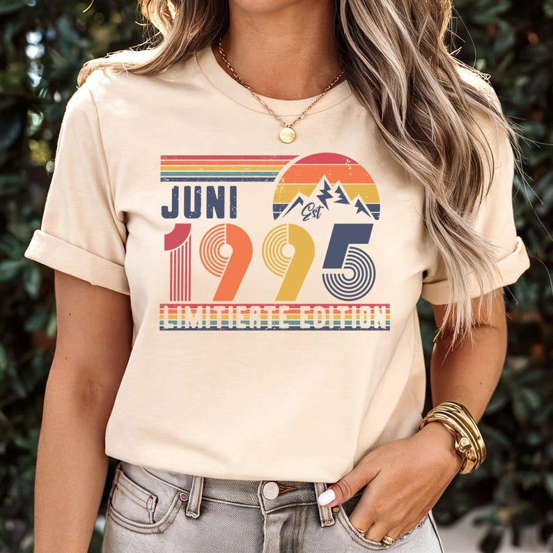 May include: Cream-colored t-shirt with a retro design featuring the word "JUNI" above the numbers "1995" in a colorful, vintage style. The design includes a mountain graphic and the text "LIMITED EDITION".