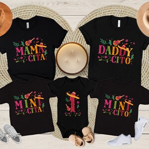 May include: A set of four black t-shirts with a festive Mexican theme. The shirts feature the text "Mama Cita", "Daddy Cito", and "Mini Cito" with a guitar, sombrero, and floral design.