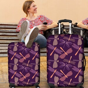 May include: Two purple luggage covers with a dragonfly pattern. The dragonflies are outlined in gold and have pink accents.