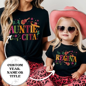 May include: Two black t-shirts with a colorful Mexican-inspired design. The larger shirt says "Auntie Cita" and the smaller shirt says "Regina".