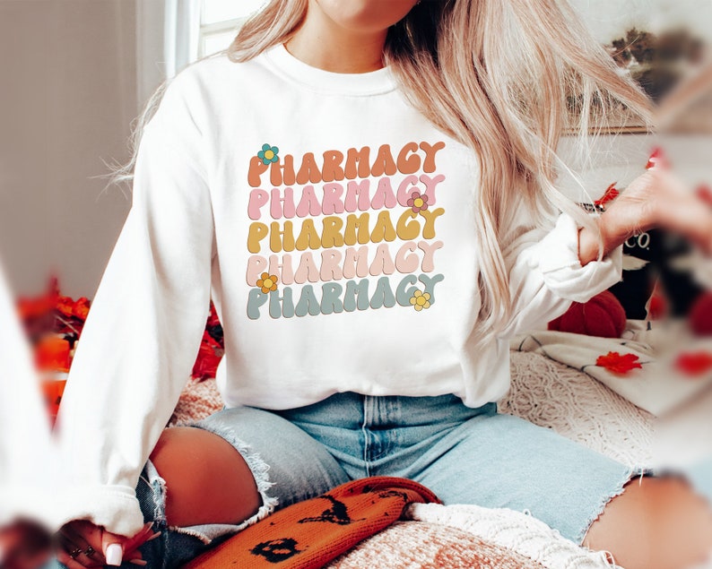 May include: White sweatshirt with the word "Pharmacy" repeated five times in a retro font with different colored flowers next to each word.