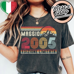 以下が含まれることがあります： レトロなデザインの濃いグレーのTシャツ。「MAGGIO」の文字と数字「2005」、テキスト「EDIZIONE LIMITATA」がデザインされています。山岳グラフィックと夕焼けをイメージした配色が特徴です。
